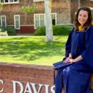 Picture of Amanda in her graduation gown sitting on a brick wall that says UC DAvis