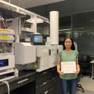 Picture of Yu-Ping holding a certificate standing in front of the LC-Q-ToF in the Barile Lab